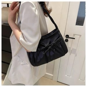 Detail of black pleated shoulder bag with drawstring bow on a model in a white blazer