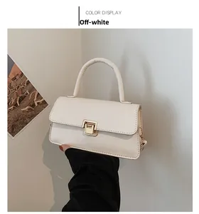 Detail einer cremeweißen Handtasche mit goldenem Drehverschluss und rundem Tragegriff