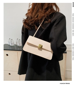Dettaglio della borsa a tracolla in pelle beige con fibbia dorata indossata da modella