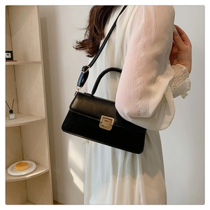 Detail of minimalist black crossbody bag with golden square lock and top handle