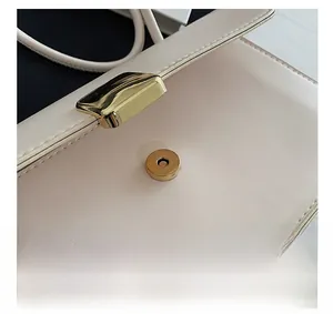 Dettaglio della chiusura magnetica dorata su borsa a tracolla beige testurizzata