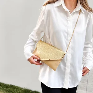 Close-up of champagne gold sequin envelope bag with V-shaped flap and fine metal chain