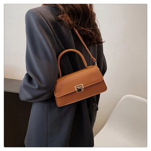 Braune Retro-Lederhandtasche mit Goldschloss am Modell in grauem Blazer getragen