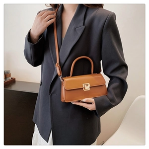 Close-up of retro brown crossbody bag with gold buckle on a model in a grey blazer