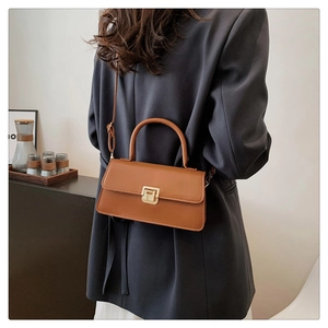 Detail of a brown leather square crossbody bag with a gold lock on a dark suit
