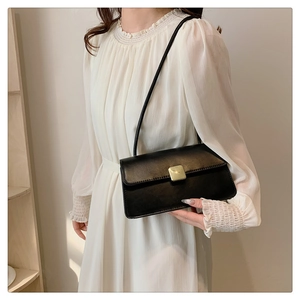 Détail d'un sac rectangulaire noir élégant avec fermoir doré sur une robe blanche