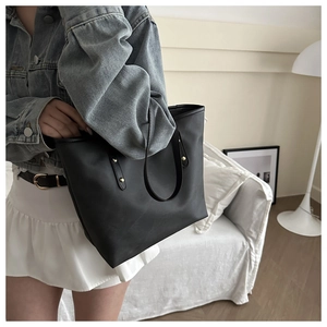 Detail of a black faux leather tote bag featuring gold stud accents worn over the shoulder