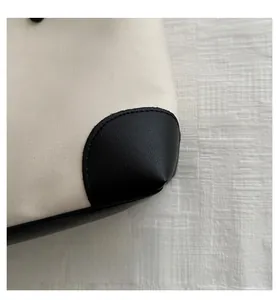 Detailed close-up of beige canvas bag with reinforced black leather corner and neat stitching