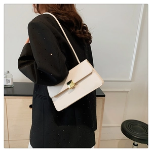 Détail d'un sac à bandoulière rectangulaire beige avec boucle dorée porté par un mannequin