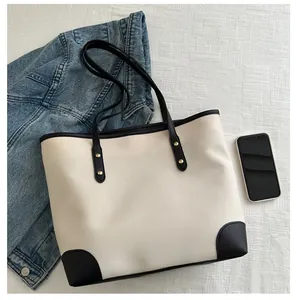 Detail of canvas tote bag with black trim, gold rivets, and a mobile phone for size reference