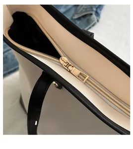 Detail of smooth gold zipper and black contrast trim on cream leather tote bag