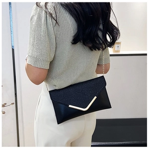 Detail of black glitter envelope clutch with gold V-metal trim worn with a chain strap