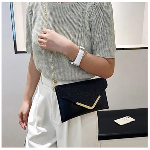 Detail of black glitter envelope clutch with golden V-shaped metal trim and chain strap