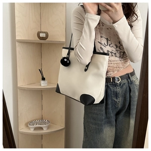 Detail of white canvas tote bag featuring black leather trim and monster charm