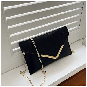 Detail of black glitter evening clutch with gold V-shape metal trim and chain strap