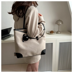 Detailed view of beige canvas tote bag with black leather trim and cute monster charm