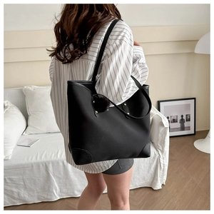 Large black tote bag with faux fur pom-pom detail on a model in a modern home setting
