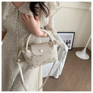 Detail of woven straw bag with floral embroidery and white leather flap closure