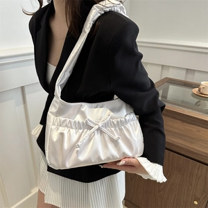 White satin pleated shoulder bag with drawstring bow detail worn by a model in a suit