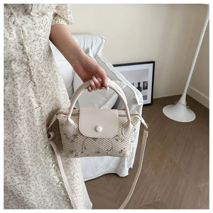 Detail of hand-woven straw handbag with floral embroidery and white PU leather strap