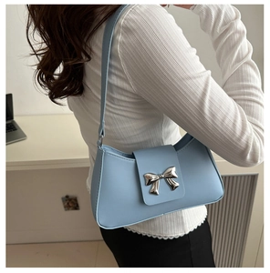 Detail of light blue PU leather crescent bag with silver metallic bow and slim strap