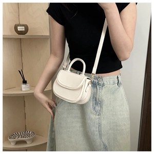 Detail of cream leather crossbody saddle bag with top handle and gold-tone hardware buckle