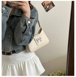 Mirror selfie showing the cream PU leather shoulder bag with silver bow detail on model