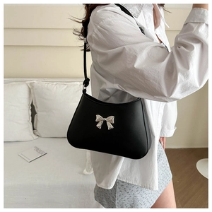 Detail of matte black shoulder bag featuring a metallic silver bow on a curved body