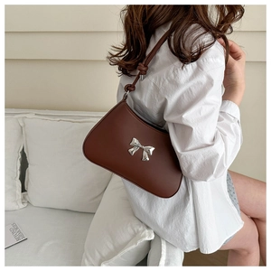 Detailed side view of brown leather underarm bag with silver bow and knotted strap