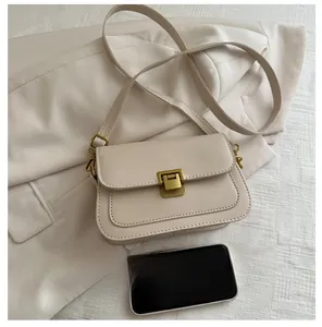 Close-up of beige square crossbody bag with gold lock next to a smartphone for size