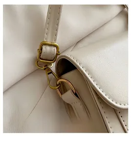 Close-up of adjustable light gold metal hook and leather strap on beige saddle bag