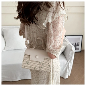 Close-up of woven cream handbag with green floral embroidery held by a model