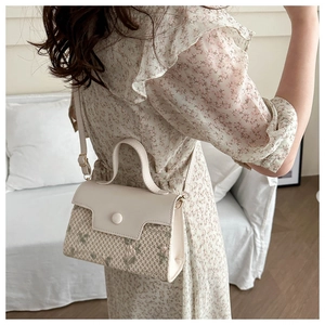 Detail van de crossbodytas van bloemenstof en crème leer over de schouder gedragen