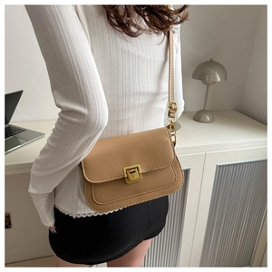 Lifestyle shot of a khaki minimalist square crossbody bag with gold buckle on desk