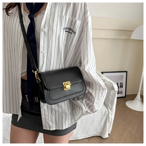 Detail of a minimalist black leather crossbody bag with a square golden metal buckle