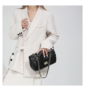 Close-up of black quilted small square bag with golden chain strap and metal turn-lock