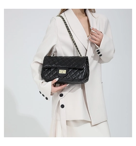 Detail of black quilted shoulder bag with gold chain strap worn with white suit jacket