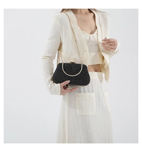 Detail of black glitter evening clutch featuring a gold semicircular handle and chain