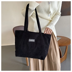 Detailed texture of black corduroy tote bag featuring a stitched fashion logo patch