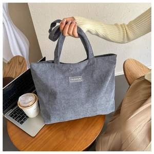 Detail of grey corduroy tote bag showing fine ribbed texture and decorative fashion label
