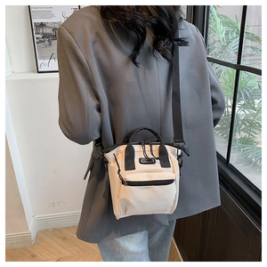 Détail du mini sac en toile beige avec sangles noires porté par un mannequin