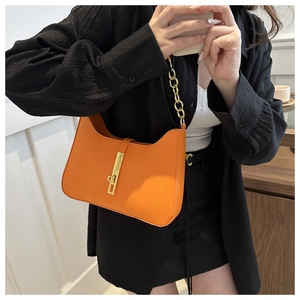 Detail of orange leather underarm bag with gold metal clasp and chain strap on model