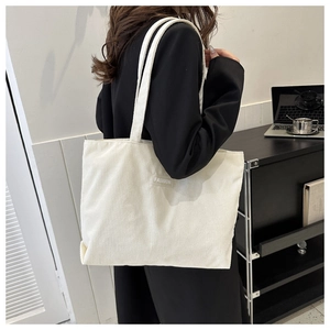 Detail of off-white corduroy tote bag showing the fashion label and fabric texture