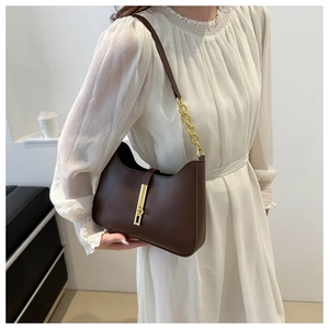 Detail of dark brown matte leather shoulder bag with gold clasp and chain on white dress