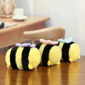 Three cute plush bee keychains with colorful wings on a warm wooden background