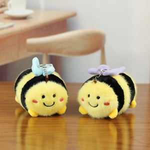 Close-up of cute plush bee keychains with heart wings on a natural wooden desk