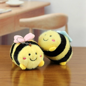 Detailed macro view of soft plush bee keychains with pink and blue wings on wood
