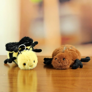Detailed close-up of fluffy bee and spider plush keychains on a rustic wooden desk