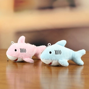 Cute plush shark keychain pendants in pink and blue colors on a wooden background