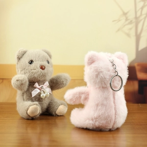 Plush teddy bear keychain with pearl accent and pink bow on a warm wooden background